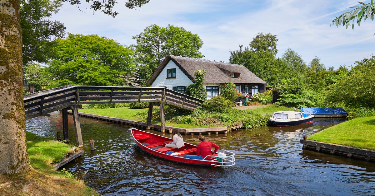 Red whisper boat carrying passengers under a wooden footbridge in Giethoorn