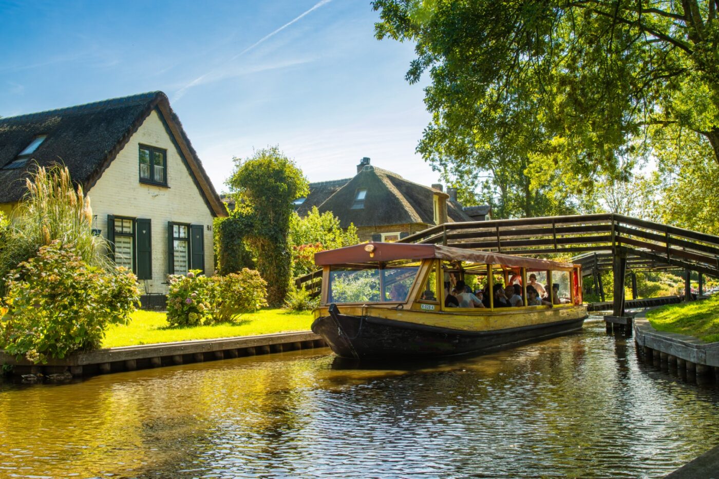 Tour boat full of passengers cruising a Giethoorn canal beside a white thatched cottage