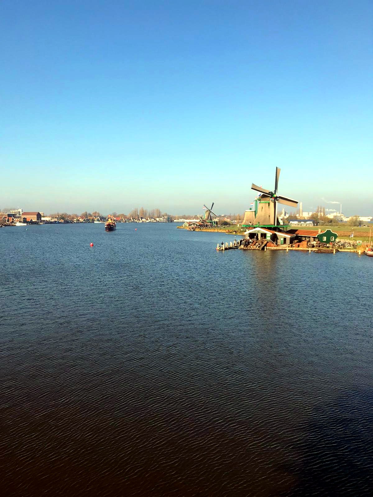 Windmill on the riverbank at Zaanse Schans under a clear blue sky