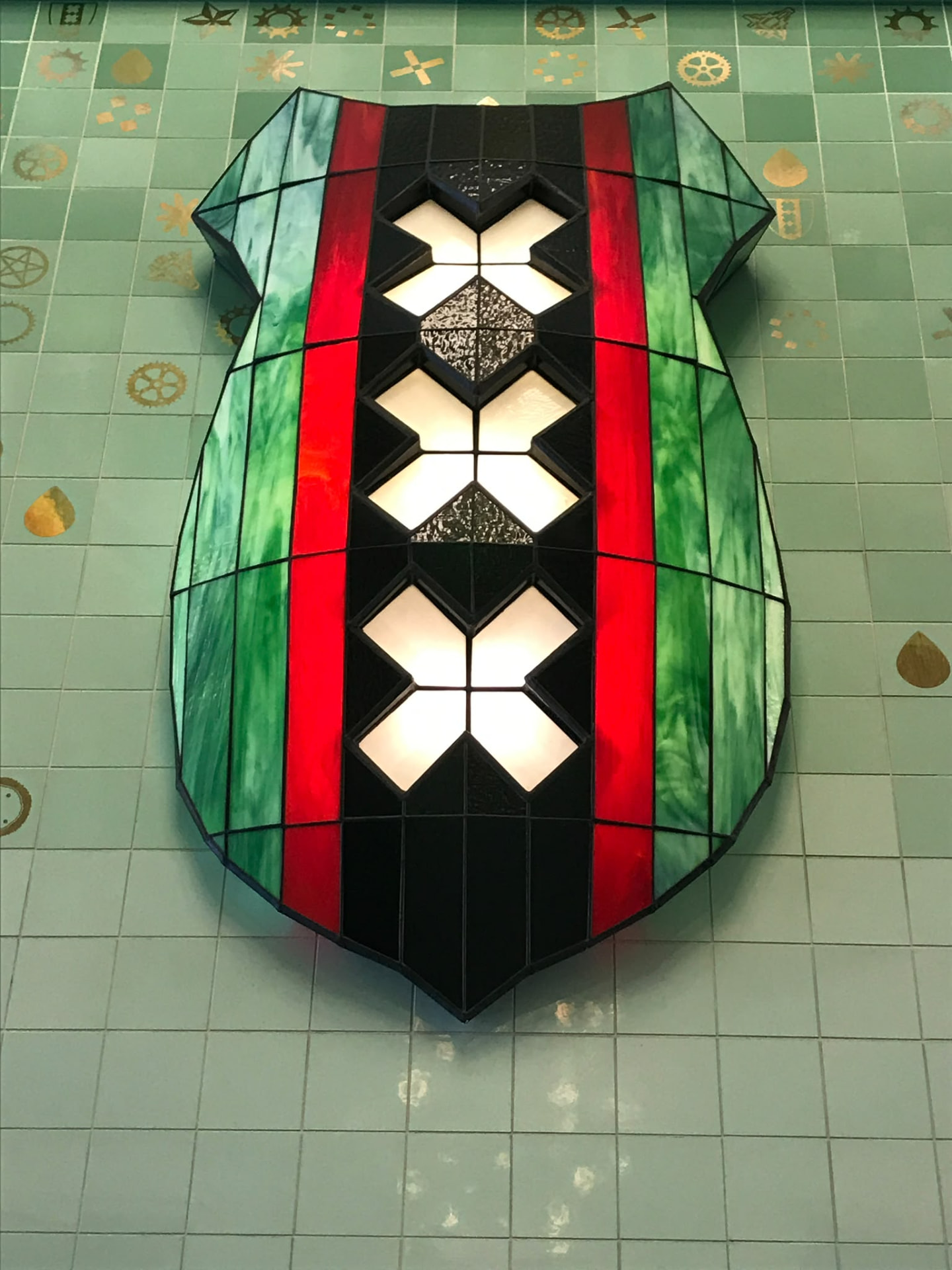 Stained-glass Amsterdam crest with three white crosses on a tiled wall