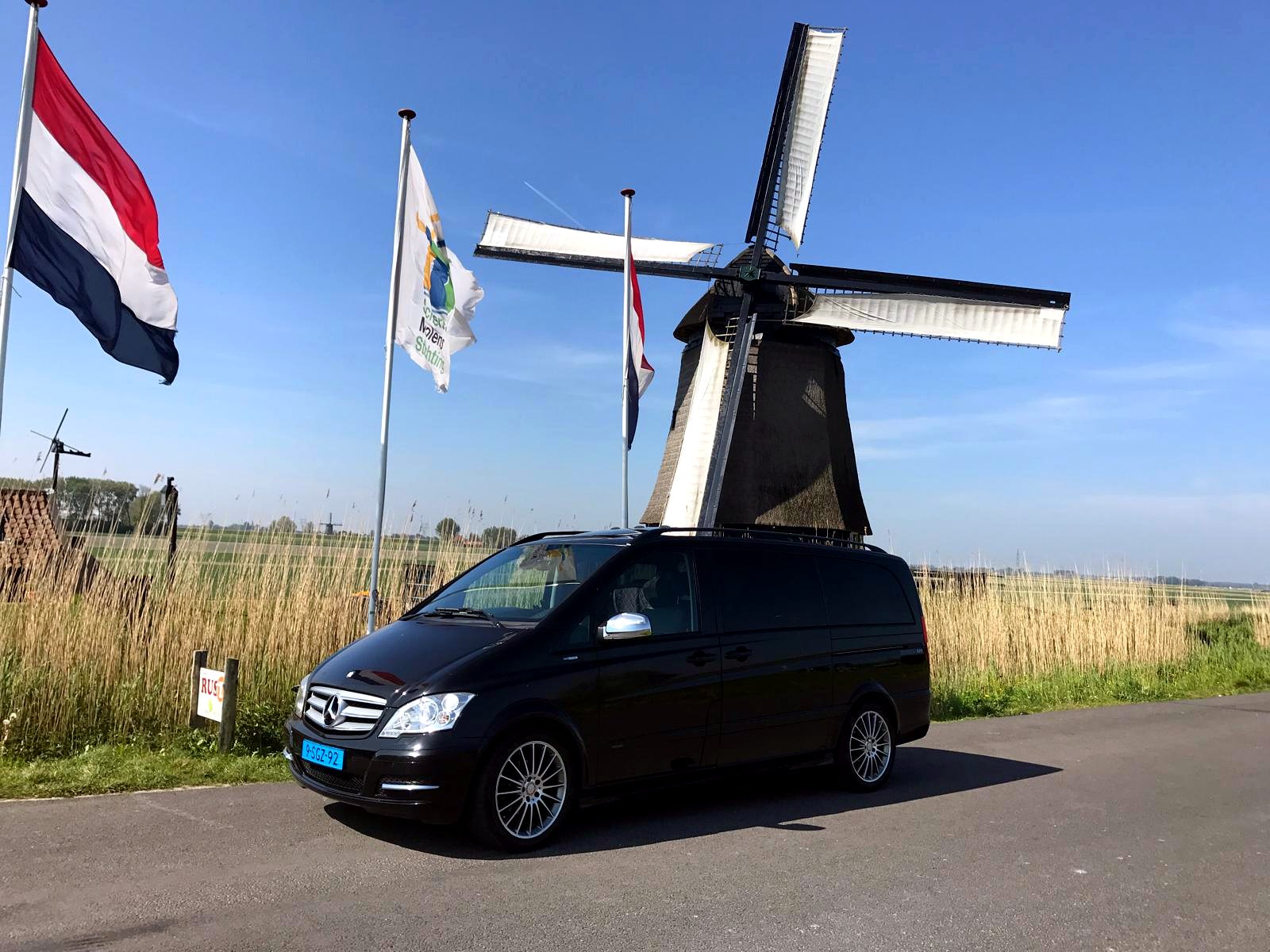 Our black Mercedes tour van parked beside a thatched windmill and Dutch flags
