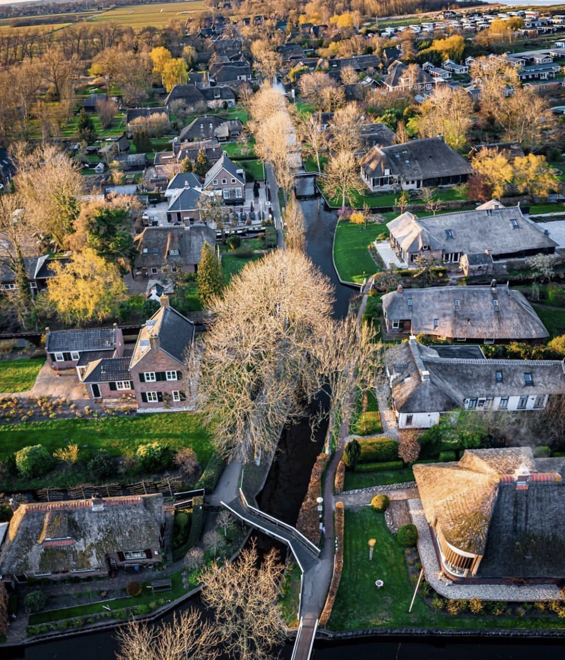 Aerial view of Giethoorn at golden hour with thatched cottages and wooden bridges along the canal