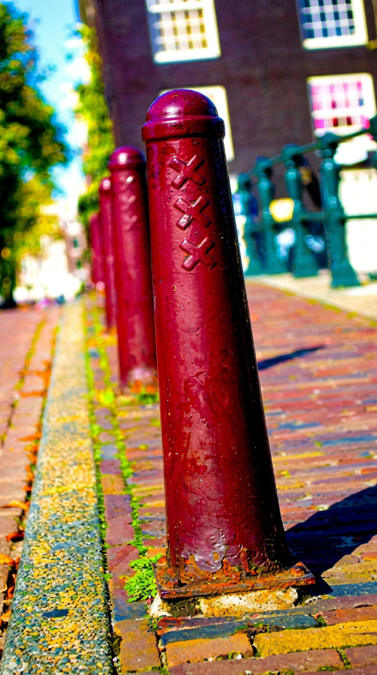 Row of red Amsterdammertje bollards with the city's three-cross coat of arms along a canal